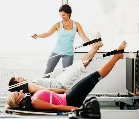 Klinik pilates eğitmeni eşliğinde reformer pilates yapan iki kişi