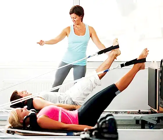 Klinik pilates eğitmeni eşliğinde reformer pilates yapan iki kişi
